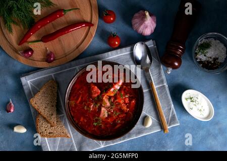 Draufsicht auf die traditionelle beliebte russische Suppe Borscht aus Kohl, Rüben und anderem Gemüse, serviert auf einer Tonerde mit Sauerrahm Stockfoto