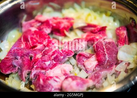 Rote, rohe Lammfleisch-Schulterkoteletts in der Pfanne über Zwiebeln geschnitten, um traditionelle kasachische oder usbekische Pilaf oder Plov-Makro-Nahaufnahme zu machen Stockfoto