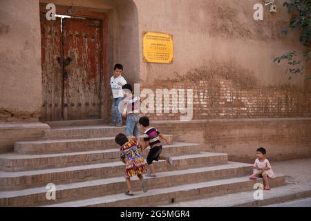 Fünf Kinder spielen auf einer Treppe, die zu einem alten verwitterten Holztor führt Stockfoto