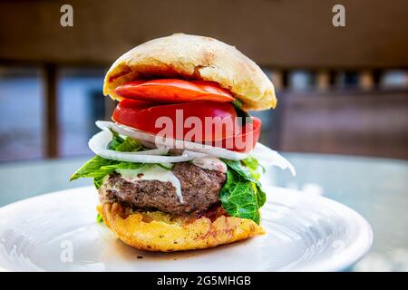 Hoher kleiner Burger-Slider stapelte Lebensmittel mit geschmolzenem Käse, Tomaten und Salat auf weißem Teller, Makroansicht aus der Nähe Stockfoto