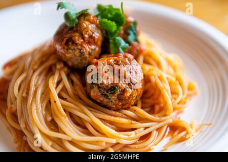 Nahaufnahme von roten Tomatensoße italienische Pasta-Nudeln und Koriander auf weißem Teller als italienisches Gericht Makro Nahaufnahme mit Textur auf Fleisch Stockfoto