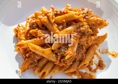 Nahaufnahme von flacher Oberseite Blick auf frische rote Tomatensauce Marinara und gemahlenes Lamm oder Rindfleisch Bolognaise mit Penne Pasta Nudeln auf weißem Teller Hintergrund Stockfoto