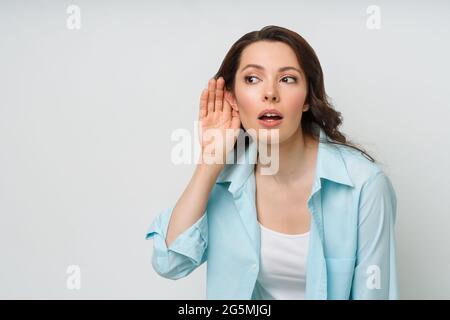 Eine junge Frau lauscht das Gespräch einer anderen Person mit der Hand ans Ohr. Das Konzept von Lauschangriffen, Spionage, Klatsch und der gelben Presse Stockfoto