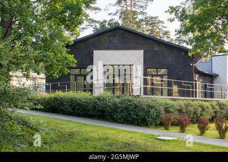 Außenansicht eines luxuriösen Privathauses. Moderne Architektur der Hütte. Grüner Rasen, Zaun und Pfad. Ein wunderschönes, schwarzes und teures Wohnhaus Stockfoto