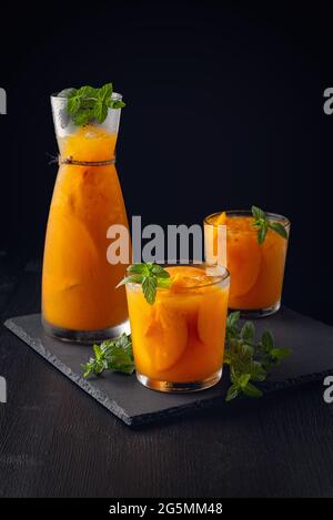 Kalte Getränke im Sommer: Hausgemachte Pfirsich-Sangria mit Eis und Minze im Glas auf schwarzem Holzhintergrundsommerliche kalte Getränke: Hausgemachte Pfirsich-Sangria mit Eis Stockfoto