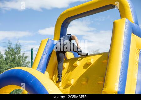 Der Typ auf der aufblasbaren Rutsche. Spaß Erholung und Sport. Wettbewerb auf einem aufblasbaren Hindernisparcours. Ein Mann klettert einen Hügel hinauf. Das Design ist mit Luft gefüllt Stockfoto