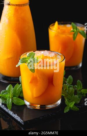 Kalte Getränke im Sommer: Hausgemachte Pfirsich-Sangria mit Eis und Minze im Glas auf schwarzem Hintergrund aus Holz Stockfoto