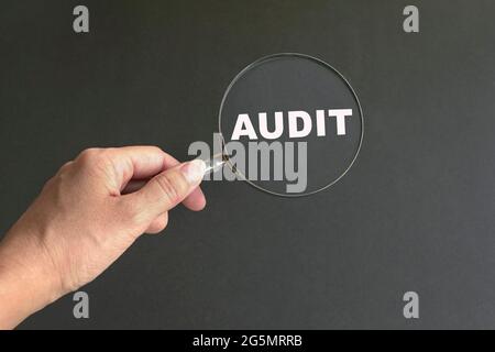 Audit, Wort auf Lupe von Hand gehalten. Schwarzer Hintergrund. Stockfoto