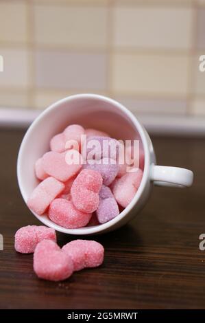 Vertikale Aufnahme von rosa herzförmigen Gelee-Bonbons in einer weißen Tasse auf einem Holztisch Stockfoto