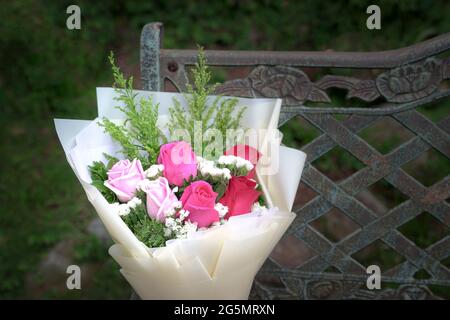 Auf einem rustikalen Stahlstuhl ruhen Bouquet aus frischen roten und rosafarbenen Rosen. Speicherplatz kopieren. Stockfoto