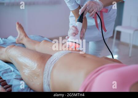 Frau erhält eine elektrische Massage gegen Cellulite. Der Arzt führt für den Patienten eine Ultraschall-Kavitationskorrektur der Körperkonturen durch. Anti Stockfoto
