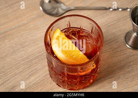 Nahaufnahme des negroni-Cocktails auf einer Holzoberfläche mit einem Rührlöffel im Hintergrund Stockfoto