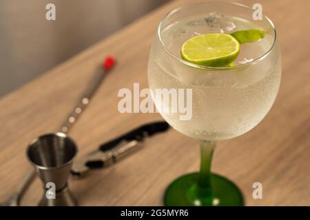 Vorderansicht von Gin und Tonic mit Zitrone und Jigger, Flaschenöffner und Mischlöffel aus dem Fokus auf Holzoberfläche Stockfoto