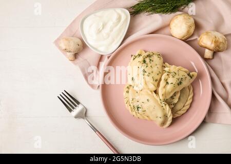 Teller mit leckeren Knödeln, Pilzen und saurer Creme auf hellem Holzhintergrund Stockfoto