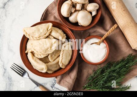 Schüssel mit leckeren Knödeln, Sauerrahm und Pilzen auf hellem Hintergrund Stockfoto