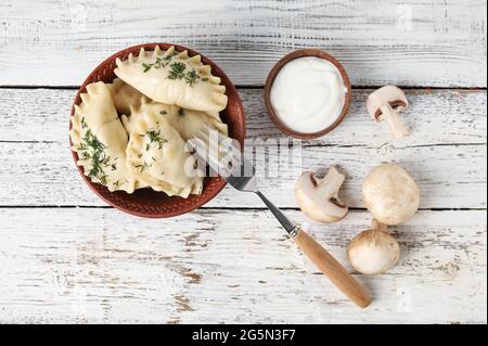 Schüssel mit leckeren Knödeln, Sauerrahm und Pilzen auf hellem Holzhintergrund Stockfoto