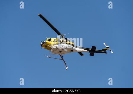 Ein Hubschrauber vom Typ Bell 205-A1, der für die Feuerunterdrückung aus der Luft konfiguriert ist, mit einem flexiblen Schlauch zum Befüllen und Fallenlassen von Wasser im Feuer. Stockfoto