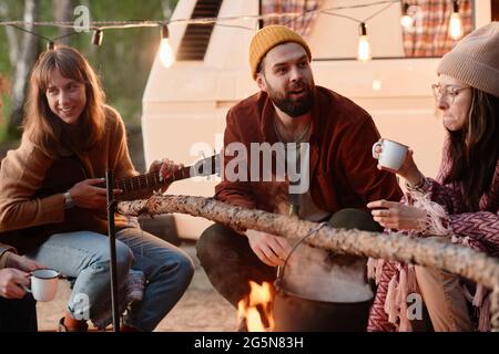 Eine Gruppe von Freunden, die neben dem Feuer sitzen und Tee trinken und sich bei einem Picknick unterhalten Stockfoto