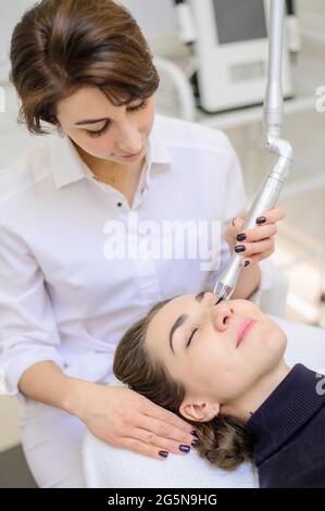 Eine Frau liegt im Büro eines Dermatologen auf einer Couch und erhält einen kosmetischen Eingriff. CO2-Schleifen der Gesichtshaut mit Hilfe eines Stockfoto