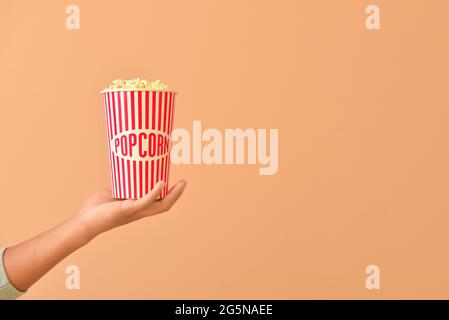 Männlicher Hand-Eimer mit Popcorn auf farbigem Hintergrund Stockfoto