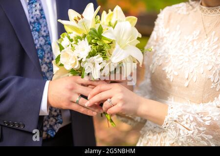 Hände eines jungen frisch verheirateten Paares mit Blumenstrauß aus weißen Lilien, die Eheringe zeigen Stockfoto