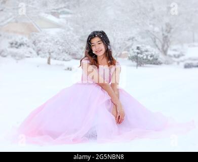 Biracial Teenager-Mädchen in langen formellen rosa Kleid sitzt im Freien in schönen Schneefall Stockfoto