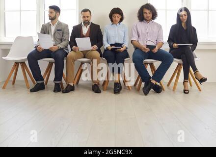 Junge Geschäftsleute Männer und Frauen mit Dokumenten vor einem Arbeitstreffen sitzen in Bürostühlen im Flur Stockfoto
