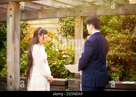 Biracial Braut lächelt während der Hochzeit im Freien unter Pergola während der Gelübde Stockfoto