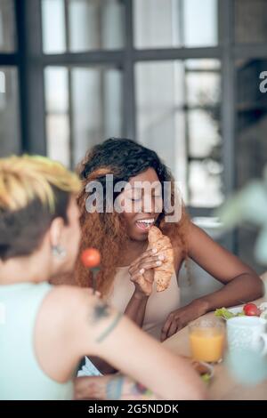 afroamerikanische Frau mit Croissant in der Nähe von offenem Mund Stockfoto