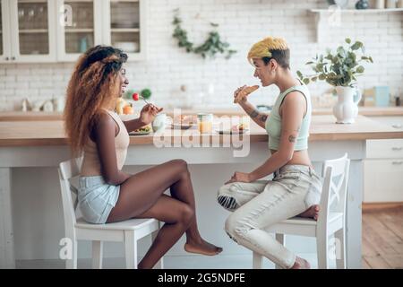 Zwei glückliche Freundinnen essen einander gegenüber Stockfoto