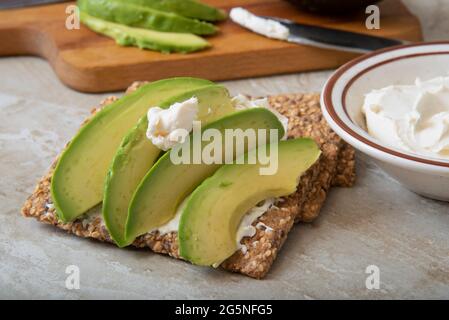 Avocado-Scheiben und Frischkäse auf gesunden Gourmet-Knäckebrot-Crackern Stockfoto