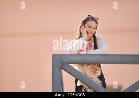 Nette junge Frau steht auf dem Balkon und redet am Telefon Stockfoto