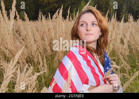 Eine Erwachsene Frau mit US-Flagge geht im Herbstgras in der Natur spazieren Stockfoto