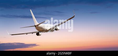 Passagiere Verkehrsflugzeug fliegen über Wolken in Sonnenuntergang Licht. Konzept für schnelle Reisen, Urlaub und Business. Stockfoto