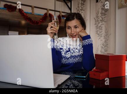 Glückliche asiatische Frau trägt blauen Pullover mit einem Glas Champagner, im Gespräch mit der Familie, soziale Distanz Freund von Videokonferenz Gespräch Gespräch ein Stockfoto