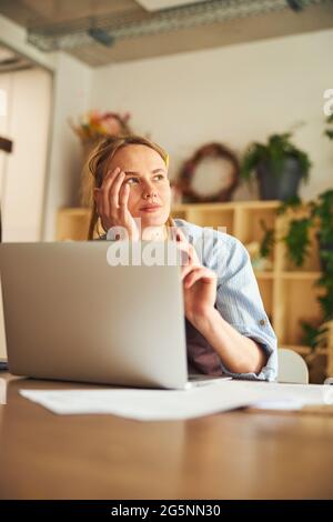 Nachdenklicher Florist sitzt am Laptop in der Werkstatt Stockfoto