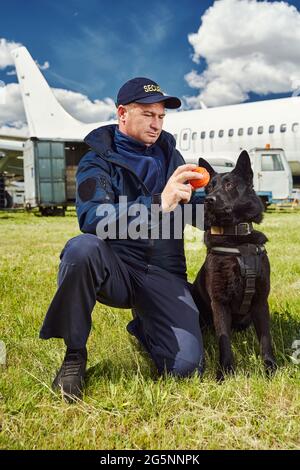 Männlicher Sicherheitsbeamter, der den Erkennungshund auf dem Flugplatz trainiert Stockfoto