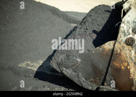 Baggereimer mit Asphalt. Asphalt auf der Straße legen. Ein Eimer mit Baumaterial. Stockfoto
