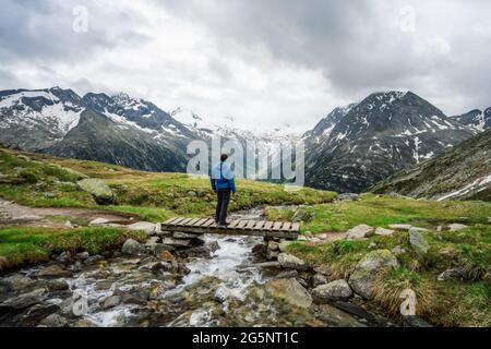 Mann Wanderer auf kleiner Brücke über Berg Fluss am Schlegeis See, Zillertaler Alpen, Österreich ruhen Stockfoto