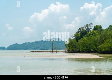 Meeresblick auf einen tropischen Strand bei Ebbe mit weißem Sand, Bäumen, türkisfarbenem Meer gegen blauen Himmel mit Wolken am sonnigen Sommertag. Landschaftlich reizvolle Landschaft Stockfoto