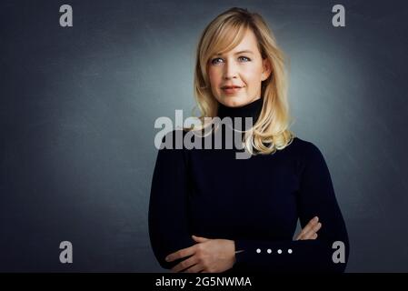 Porträtaufnahme einer attraktiven blonden Frau, die mit gekreuzten Armen auf einem isolierten grauen Hintergrund steht. Speicherplatz kopieren. Stockfoto