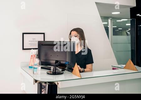 Junge Frau trägt Gesichtsmaske aufgrund covid19 als Rezeptionistin in der Zahnklinik. Stockfoto