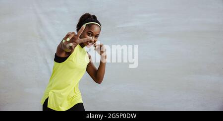 Glückliche Frau in Sportswear gestikuliert Friedenszeichen. Weibliche Athletin, die eine Pause vom Training mit Siegessieg-Handzeichen einnahm. Stockfoto