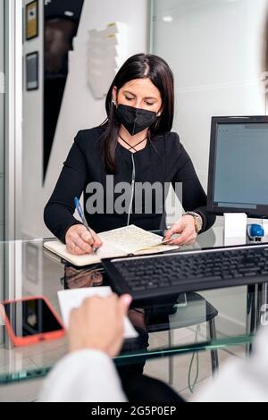 Junge Zahnärztin, die Gesichtsmaske trägt, weil sie in ihrem Büro arbeitete und sich Notizen machte. Stockfoto