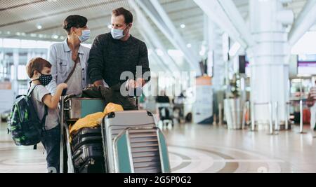 Ehemann und Ehefrau schauten einander an, während das Kind während einer Pandemie auf dem Gepäckwagen am Flughafen stand. Familie, die während einer Pandemie am Flughafen wi reist Stockfoto