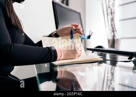 Unerkannte Zahnärztin, die Gesichtsmaske trägt, weil sie in ihrem Büro arbeitete und sich Notizen machte. Stockfoto