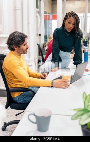 Hübsche afroamerikanische Frau, die mit ihrem reifen Kollegen im Büro arbeitet und den Computer benutzt. Stockfoto
