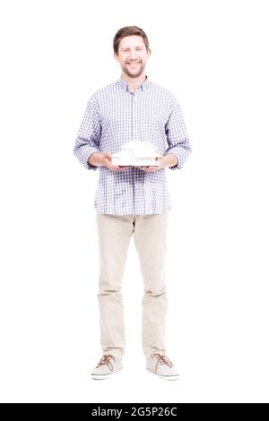 Studio-Porträt eines hübschen bärtigen kaukasischen Mannes in legerer Kleidung, der das Hausmodell in den Händen hält, weißer Hintergrund Stockfoto