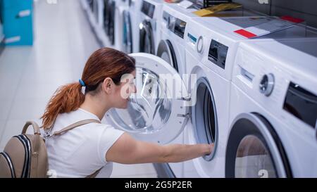 Kaukasische Frau wählt eine Waschmaschine in einem Haushaltswarenladen Stockfoto