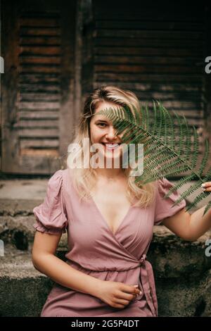 Eine junge Frau hält ein Farnblatt in ihren Händen und bedeckt damit einen Teil des Gesichts. Das Konzept der Naturkosmetik Stockfoto